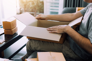 Asian entrepreneur teenager is opening a cardboard box in order to put the product that the customer ordered into the box to deliver the product.