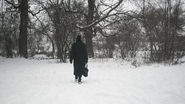 A man in a black cloak and hat walks through the woods and approaches the river bank. 60fps. 4k