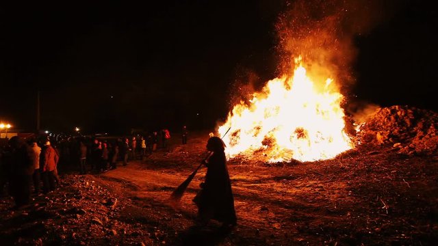 Girl disguised as a witch walking in front of traditional bonfire of Epiphany