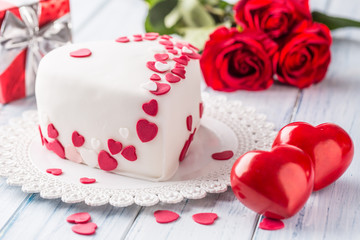 Marzipan white cake in the shape of a heart with red hearts. As the decoration bouquet of red roses a gift from the ribbon. Wedding or valentines day concept.