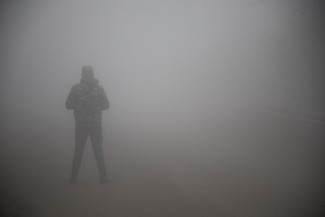 silhouette of a man standing in the foggy road.