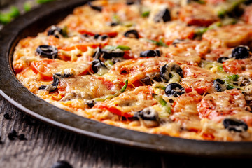 Concept of Italian cuisine, Homemade Italian pizza with salami sausage, tomatoes, with black olives and cheese on a wooden background. copy space