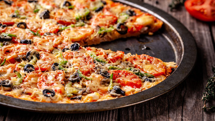 Concept of Italian cuisine, Homemade Italian pizza with salami sausage, tomatoes, with black olives and cheese on a wooden background. copy space
