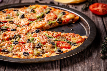 Concept of Italian cuisine, Homemade Italian pizza with salami sausage, tomatoes, with black olives and cheese on a wooden background. copy space