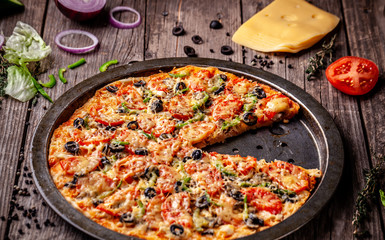 Concept of Italian cuisine, Homemade Italian pizza with salami sausage, tomatoes, with black olives and cheese on a wooden background. copy space