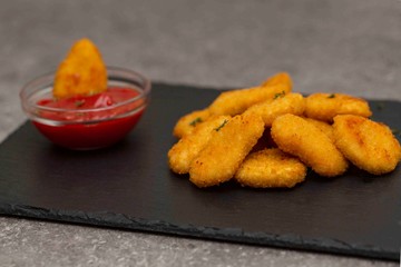 Fried crispy chicken nuggets with ketchup on black board.