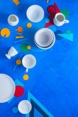 White dishes and cups on a colorful background with geometric shapes. Color block kitchenware flat lay with copy space.