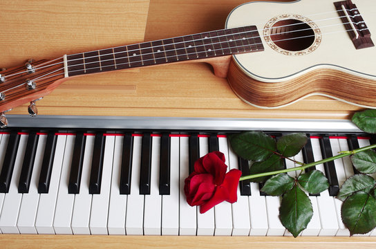 Ukulele and red rose on piano keyboard