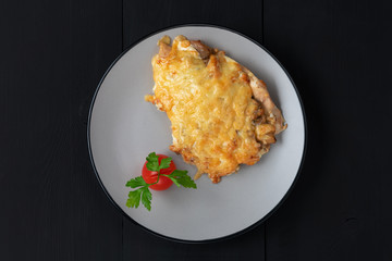 Baked chicken under cheese with tomate and parsley in grey plate on a wooden black background. Top view