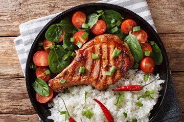 Healthy grilled pork steak with rice and fresh vegetables close-up on a plate. horizontal top view
