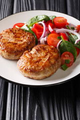 Roasted meatballs crepinette with turkey wrapped in a сaul fat, served with fresh vegetable salad close-up. vertical