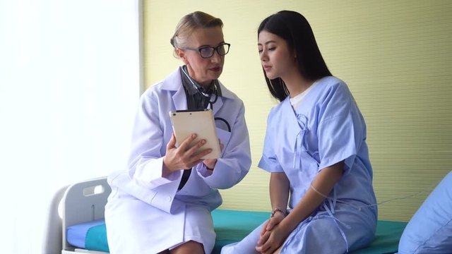 The senior female doctor is talking or explaining something to the patient and see the results of the evaluation in the patient's room.
