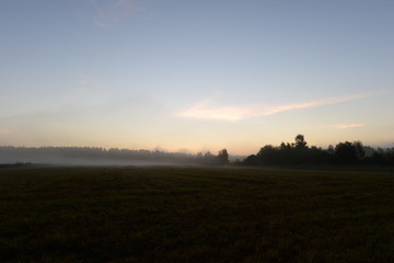 Sunlight of dawn in the blue sky above a field in the morning mist early morning.