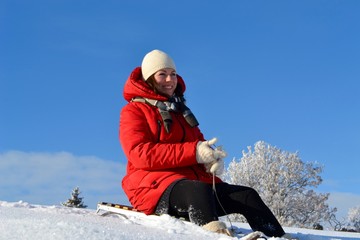 Fototapeta na wymiar Happy young beautiful woman in a bright red jacket, hat and scarf on a sled on the background of a fabulous winter landscape on the mountain 