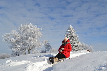 Happy young beautiful woman in a bright red jacket, hat and scarf on a sled on the background of a fabulous winter landscape on the mountain 