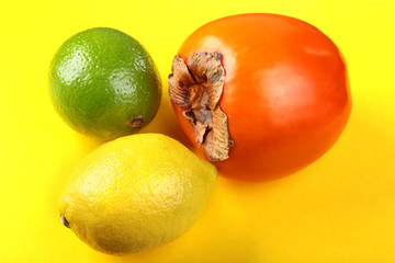Fresh mixed exotic fruits lemon, persimmon and lime on a yellow background. Fruit background. Top View.