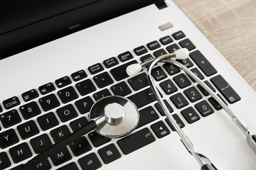 Modern medical technology and sofware advances concept. Doctor's working table with stethoscope acoustic device, laptop keyboard close up on wooden desktop. Copy space, background, top view, flat lay.