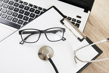 Modern medical technology and sofware advances concept. Doctor's working table with stethoscope acoustic device, laptop keyboard close up on wooden desktop. Copy space, background, top view, flat lay.