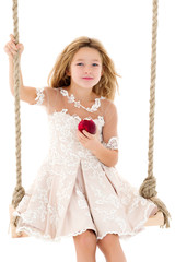 Little girl on the swing eating an apple.