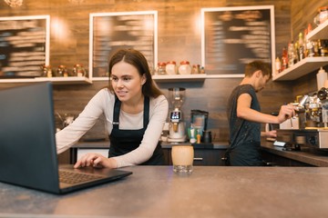 Team of coffee shop workers working near the counter with laptop computer and making coffee, cafe business