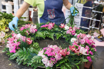 The florist creates a wreath of exotic flowers in pink tones from orchids, roses, and other flowers, herbs.