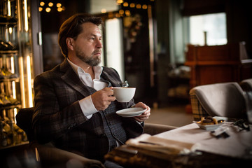 Elegant mature gentleman in stylish elegant three pieces suit, well-known woman clothes modeler having breakfast in his fafourite cafe