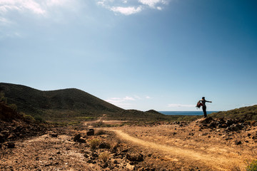 Obraz premium Happy hiker young woman with trekking backpack standing on stone in summer mountains - enjoying the desertic place with ocean in background - travel and freedom lifestyle concept