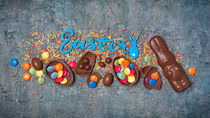 Blue text of easter with chocolate traditional eggs, bunny and sugar sprinkles or confetti