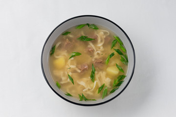 meat soup with homemade noodles, potatoes and fresh green onion on white background