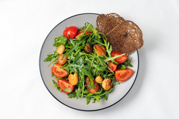 tomato salad with shrimps, arugula and rye bread crumbson a white background. Top view
