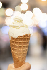Crispy cone of a milky ice cream with a bokeh of festive party lights on background.