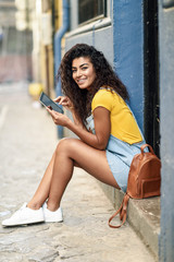 Happy Arab woman sitting on urban step with a digital tablet