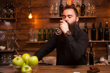Young tattooed bartender with great beard tasting a glass of wine. Hipster pub.