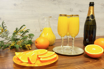 Three glasses of mimosa cocktail, a bottle of champagne, a decanter with orange juice, fresh...