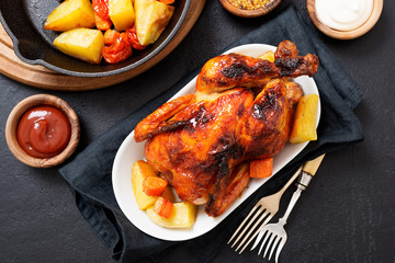 Roasted chicken with vegetables served  with sauces on dark table, top view.