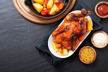 Roasted chicken with vegetables served  with sauces on dark table, top view.