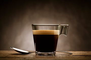 Black coffee in glass cup with teaspoon on wooden table