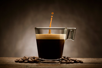 Black coffee in glass cup with coffee beans and jumping drop, on wooden table