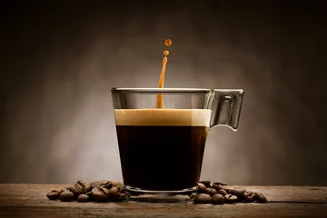 Poster Im Rahmen Schwarzer Kaffee in Glastasse mit Kaffeebohnen und springender Tropfen, auf Holztisch © winston