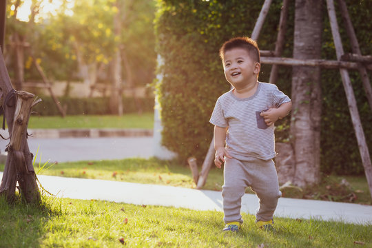 Asian Baby Boy Running In The Garden During The Evening, With The Sun Shining From The Back Of The Child