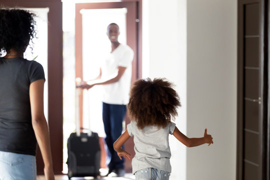 Happy Child Daughter Running To Meet African Dad Coming Home With Suitcase, Rear View At Little Kid Girl Hurrying To Hug Father Arriving After Business Trip, Welcome Back Daddy, Black Family Reunion