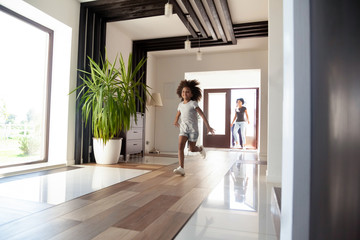 Happy little black girl running exploring big luxury house moving in, parents and excited kid daughter entering new home, cute mixed race child having fun jump in hallway, african family mortgage - obrazy, fototapety, plakaty