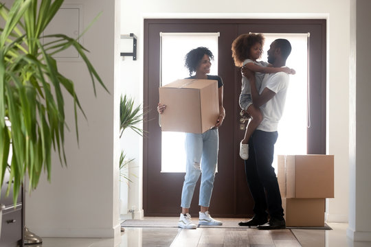Happy black family with kid girl holding box entering into own house on moving day, african american parents and child standing in hallway, mortgage, relocation, tenants welcome to new home concept