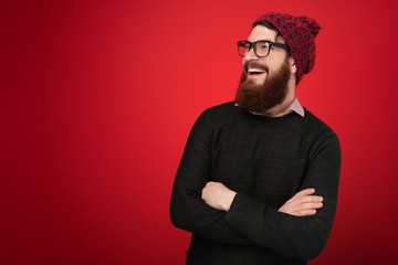 Obraz premium Smiling bearded man in sweater and red hat which posing with crossed arms and looking away