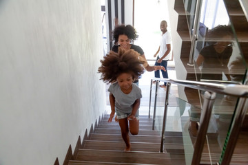 Happy african american kid girl running up stairs into new big house with black parents, excited child daughter having fun exploring own home, afro family moving day concept, relocation, mortgage © fizkes