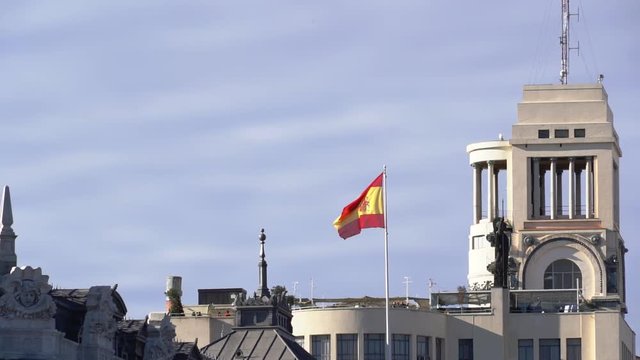 Spanish national flag in a public building roof gainst a blue and cloudy sky. Slowmotion from a 120 fps original shoot