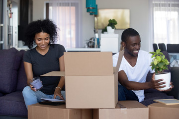 African american happy couple unpacking cardboard boxes in living room moving into new home, young black family packing stuff preparing for relocation or renovation in house or flat, removals concept