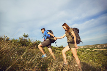 A couple of travelers with backpacks go on a road.