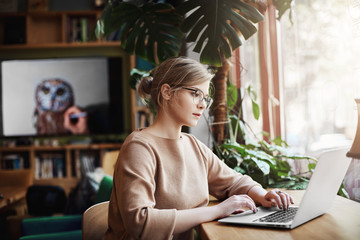 Good-looking successful fashion blogger writing new essay on laptop while sitting in cafe and...