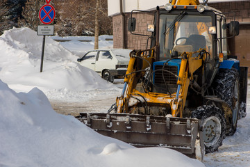 Fototapeta na wymiar The tractor removes snow. The street is full of snow drifts.